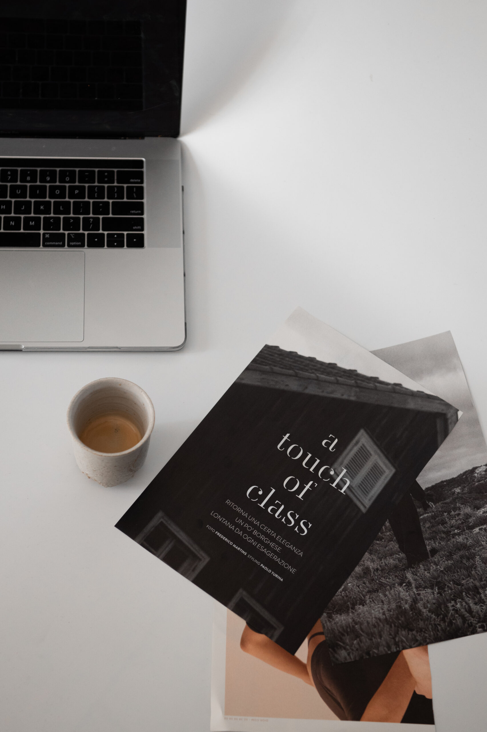 A laptop, a cup of coffee, and a magazine titled "A Touch of Class" placed on a white surface, ideal for any remote executive assistant.